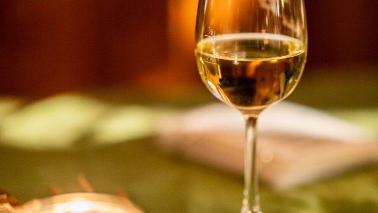 Ein Glas Wei&szlig;wein mit einer Kerze auf einem Tisch mit gr&uuml;nem Tischtuch.