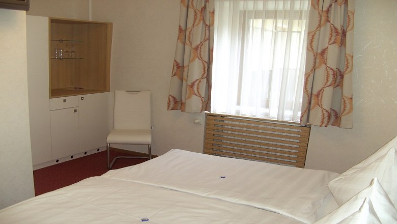 Ein Hotelzimmer mit einem Bett, einem Stuhl, einem Schrank und einem Fenster mit Vorhängen.