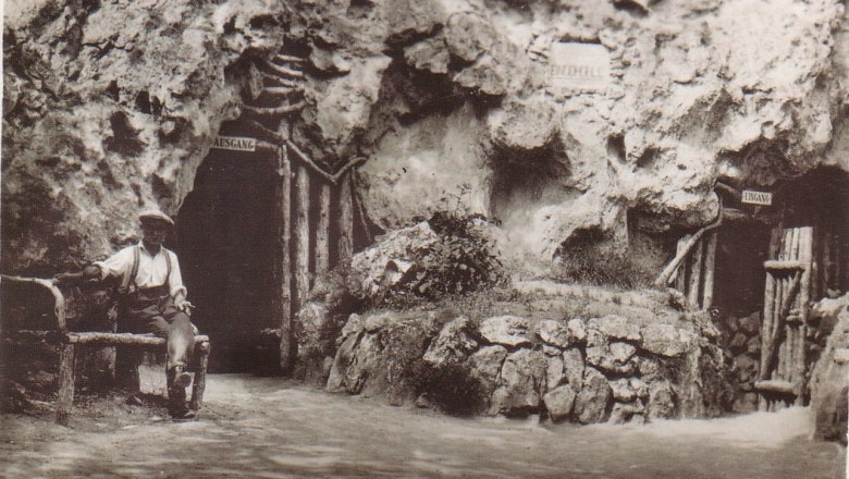 Historisches Foto der Ein&ouml;dh&ouml;hle in Pfaffst&auml;tten, Baden, mit einem Mann auf einer Bank vor dem H&ouml;hleneingang.