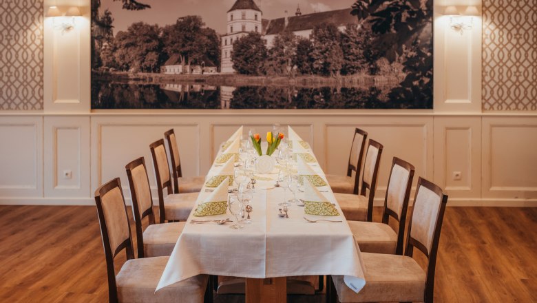Eleganter Speisesaal mit langem Tisch, gedeckt mit wei&szlig;en Tischdecken und gr&uuml;nen Servietten, im Hintergrund ein gro&szlig;es Schlossbild.