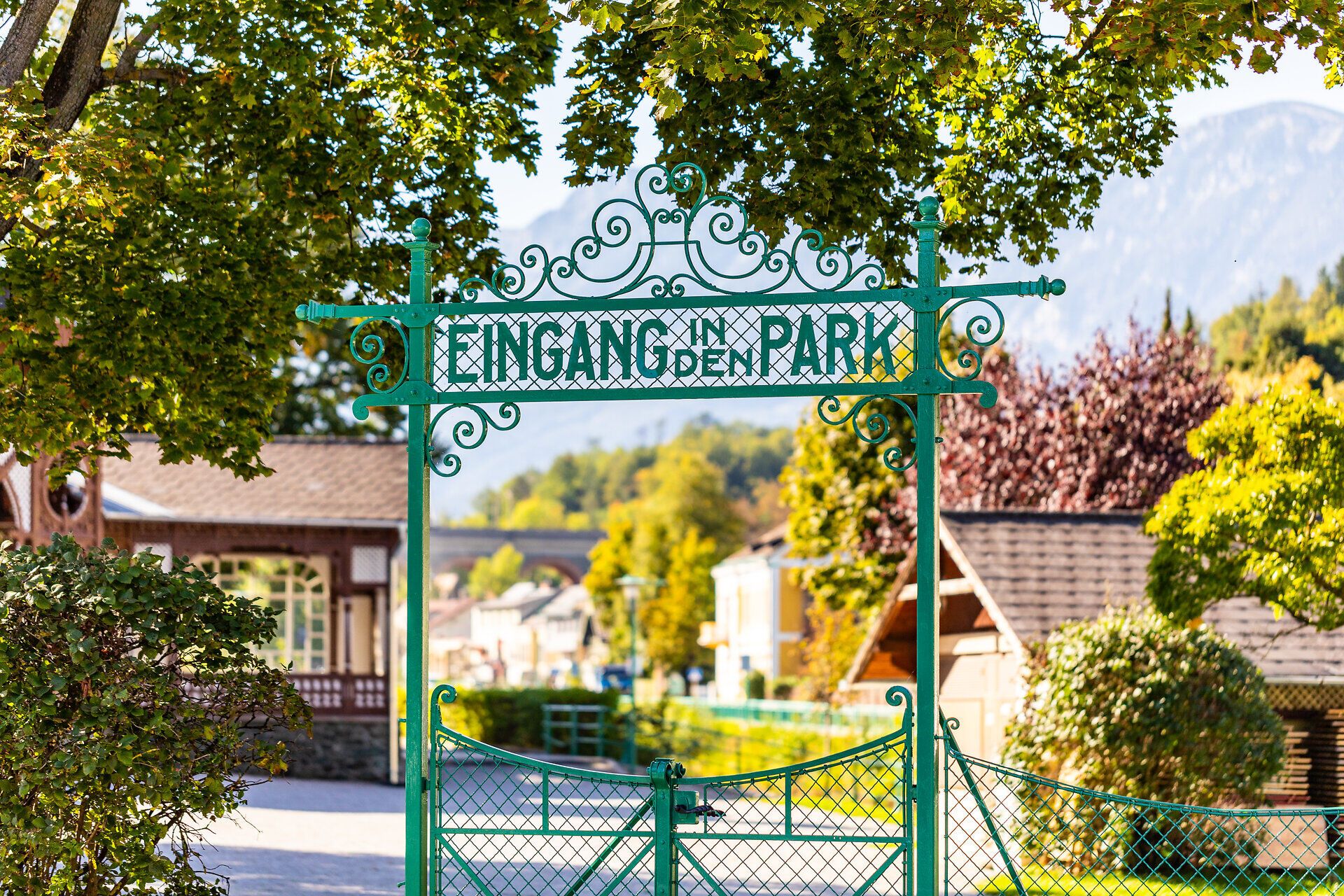 Grünes Tor mit Aufschrift "Eingang in den Park", im Hintergrund ist der Pavillon und die Rax zu sehen.