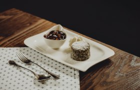 Ein Mohnkuchen mit Puderzucker, Sahne und einer Schale mit Früchten auf einem weißen Teller.
