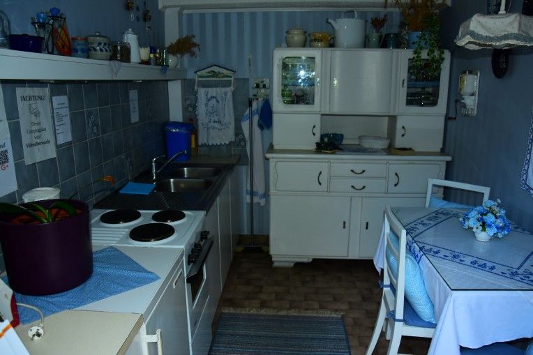 Kleine, gemütliche Küche mit blau-weißer Dekoration, einem Herd, Spüle, Schrank und kleinem Esstisch.