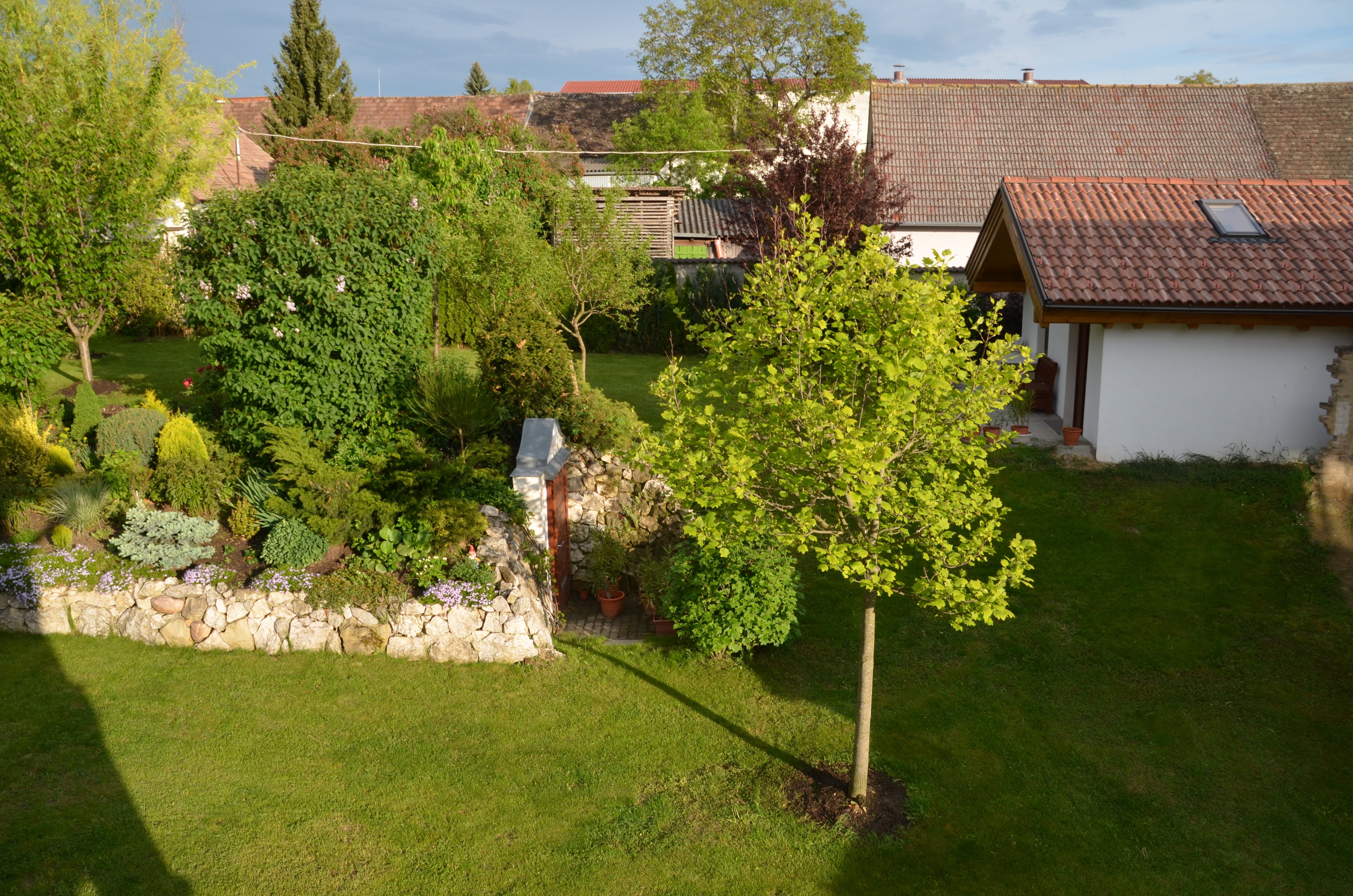 Ein gepflegter Garten mit Bäumen, Sträuchern und einem kleinen Gebäude mit Ziegeldach.
