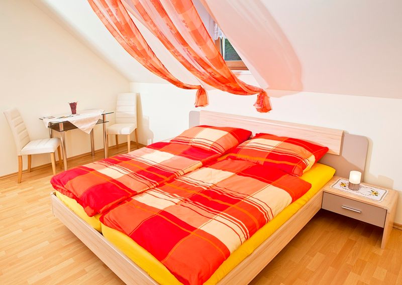 Helles Schlafzimmer mit rotem Bettbezug und dekorativen Vorhängen.