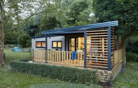 Mobilheim von außen mit Blick auf die Terrasse und erleuchtete Zimmer