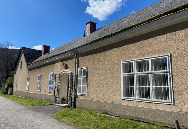 Langes, einst&ouml;ckiges Geb&auml;ude mit mehreren Fenstern und einem Schr&auml;gdach unter blauem Himmel.