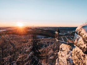 Die Wintersonne taucht die verschneite Landschaft in ein warmes Licht, w&auml;hrend die schneebedeckten B&auml;ume sanft im Wind wiegen. Ein atemberaubender Ausblick l&auml;dt dazu ein, die Ruhe der Natur zu genie&szlig;en und die frische, klare Luft einzuatmen.
