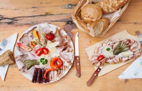 Brett mit Aufschnitt, Gem&uuml;se und Brot auf Holztisch.