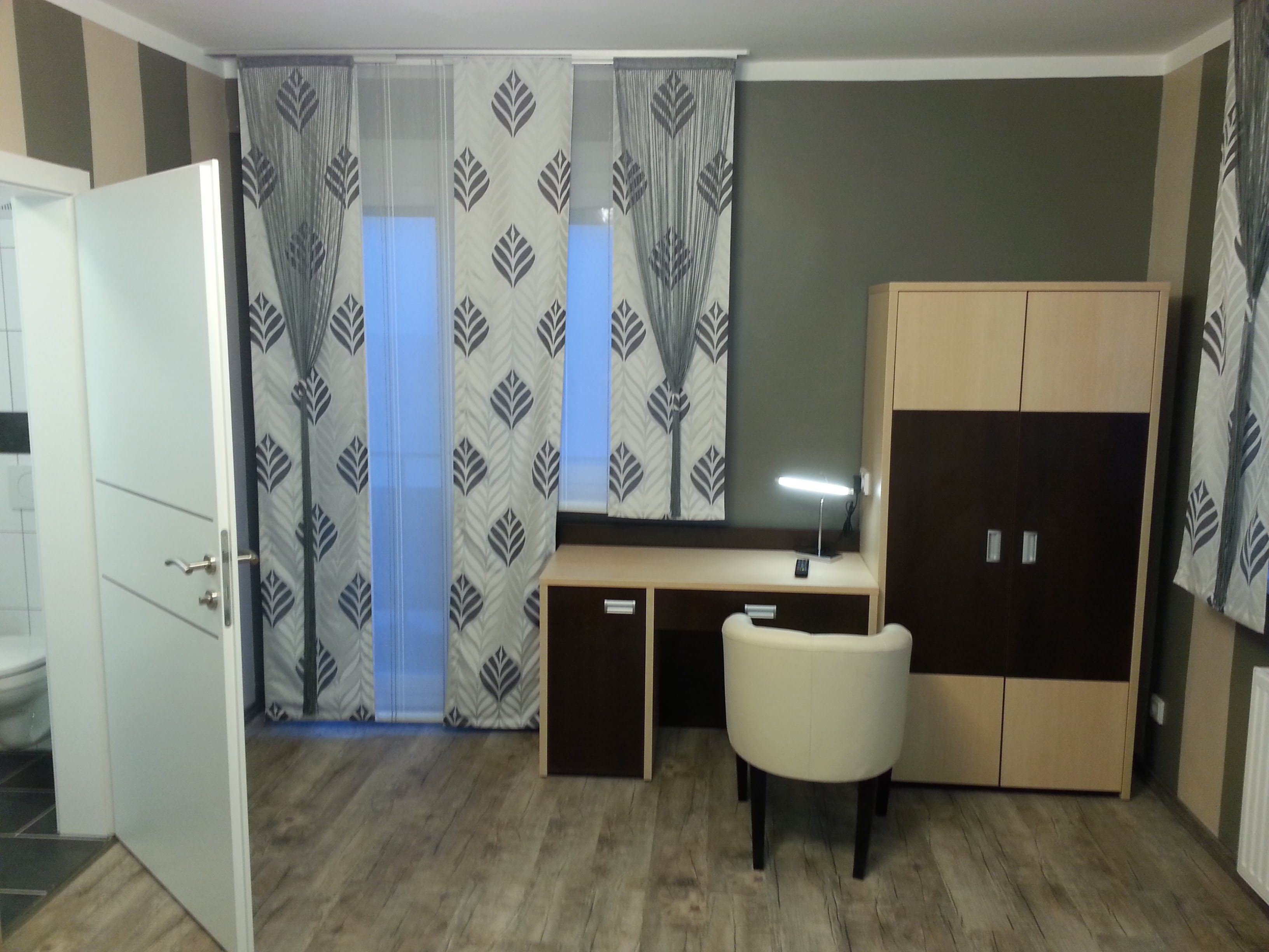 Ein modernes Hotelzimmer mit Schreibtisch, Stuhl und Kleiderschrank.