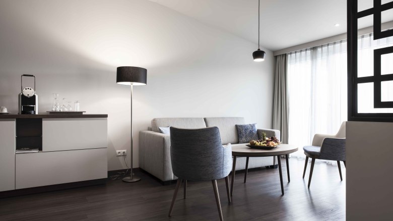 Moderne Sitzecke mit Sofa, Sessel, Tisch und Stehlampe in einem hellen Raum.