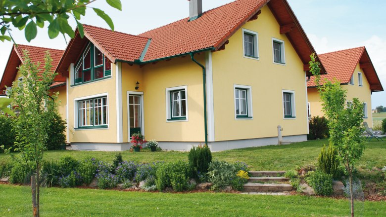 Gelbes Einfamilienhaus mit rotem Dach und gepflegtem Garten.