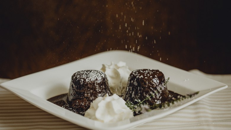 Zwei Schokoladenk&uuml;chlein mit Puderzucker und Sahne auf einem Teller.