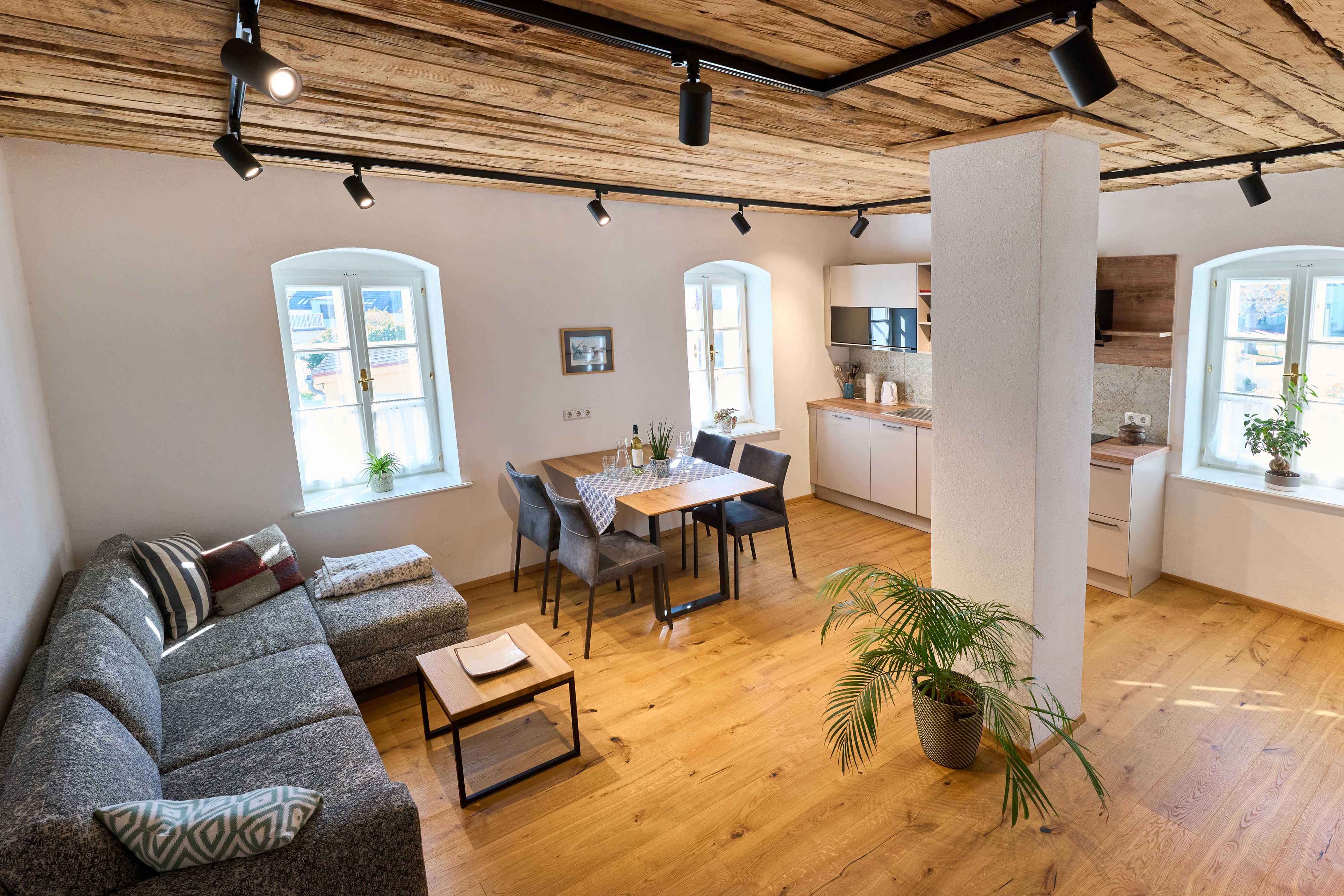 Modernes Wohnzimmer mit Holzboden, grauem Sofa, Esstisch und Küche.