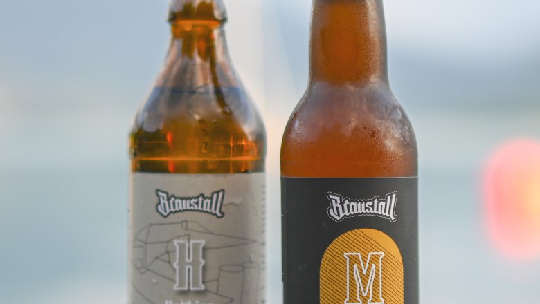 Zwei Bierflaschen von Braustall auf einem Holztisch vor unscharfem Hintergrund.