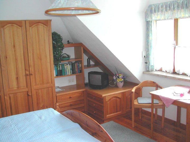 Gemütliches Gästezimmer mit Holzmöbeln, einem kleinen Fernseher, einem Tisch mit Stuhl und einem Fenster mit Vorhängen.
