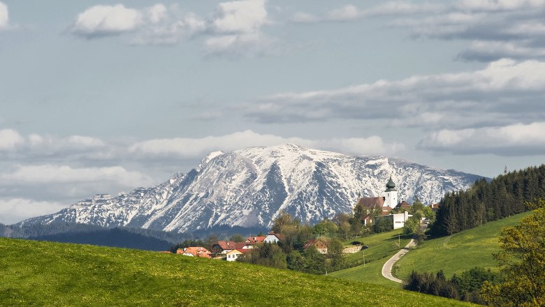 Blick auf St. Leonhard am Walde mit schneebedecktem Berg im Hintergrund.