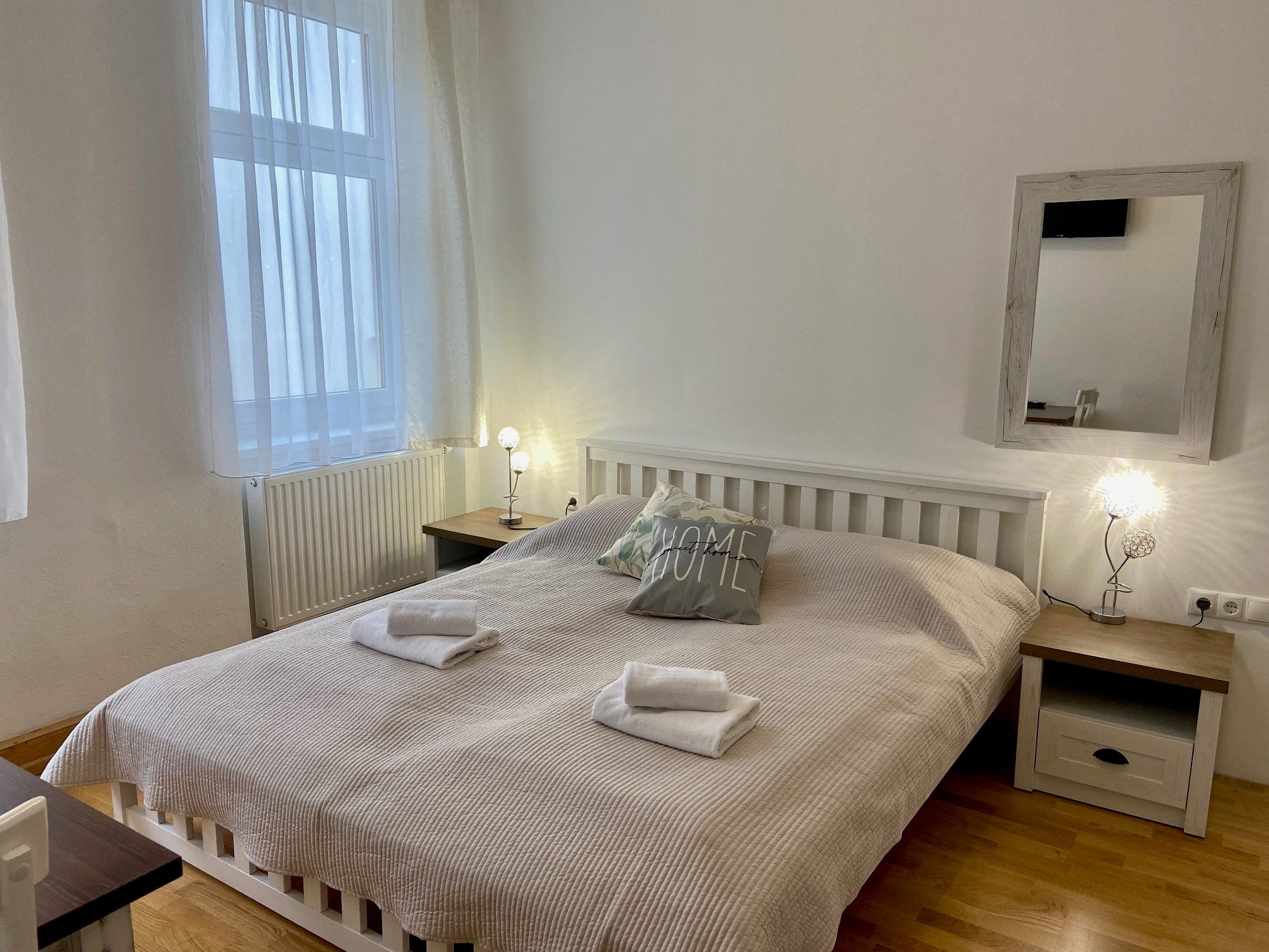 Ein gemütliches Doppelzimmer mit einem großen Bett, zwei Nachttischen und einem Spiegel an der Wand. Das Zimmer ist hell und einladend gestaltet.