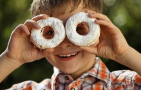 Ein Junge h&auml;lt zwei mit Puderzucker bestreute Donuts vor seine Augen.