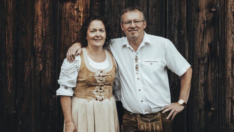 Ein Mann und eine Frau in traditioneller Tracht vor einer Holzwand.