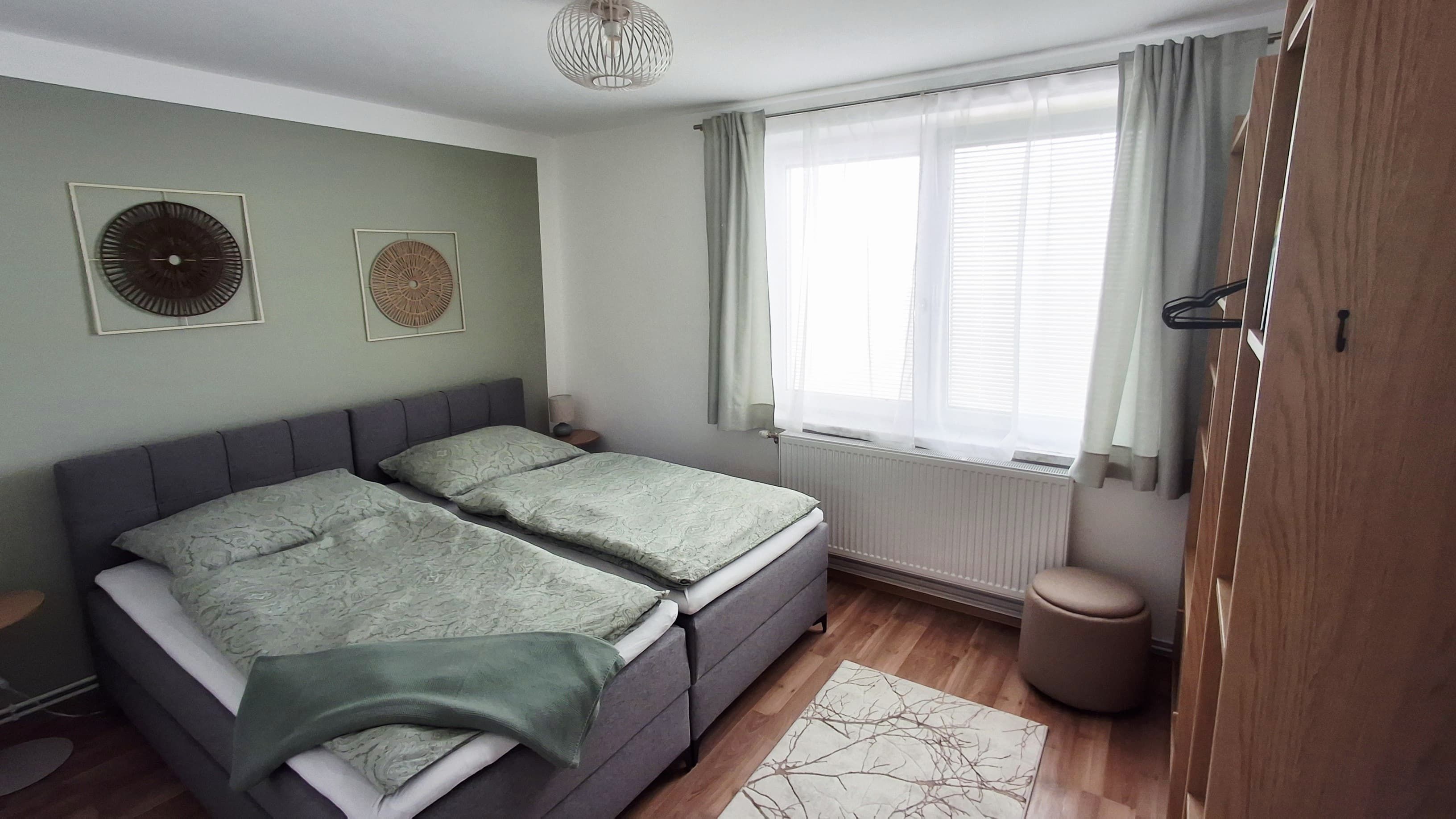 Ein gemütliches Schlafzimmer mit einem Doppelbett, grüner Bettwäsche, Holzmöbeln und dekorativen Wandbildern.