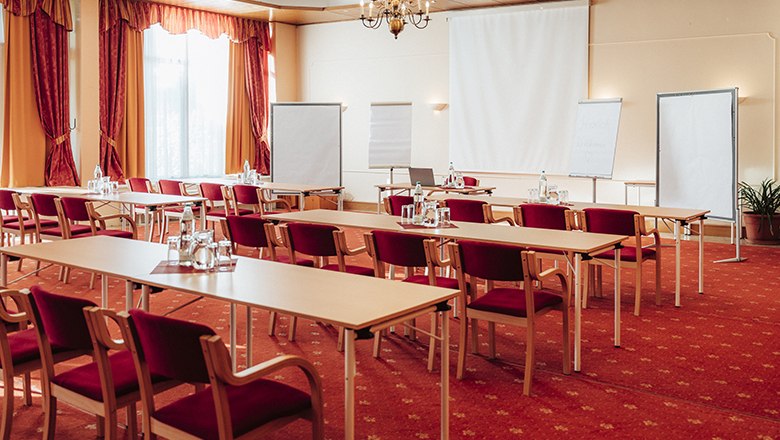 Ein Seminarraum mit roten Stühlen, Tischen, Flipcharts und einem Projektor.