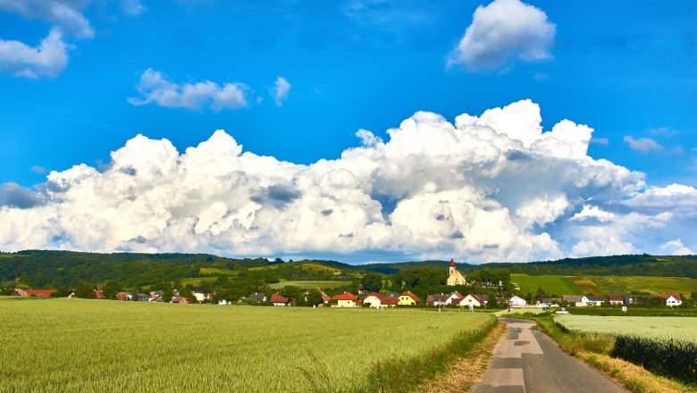 Landschaft mit Dorf, Feldern und Kirche vor gro&szlig;en Wolken.