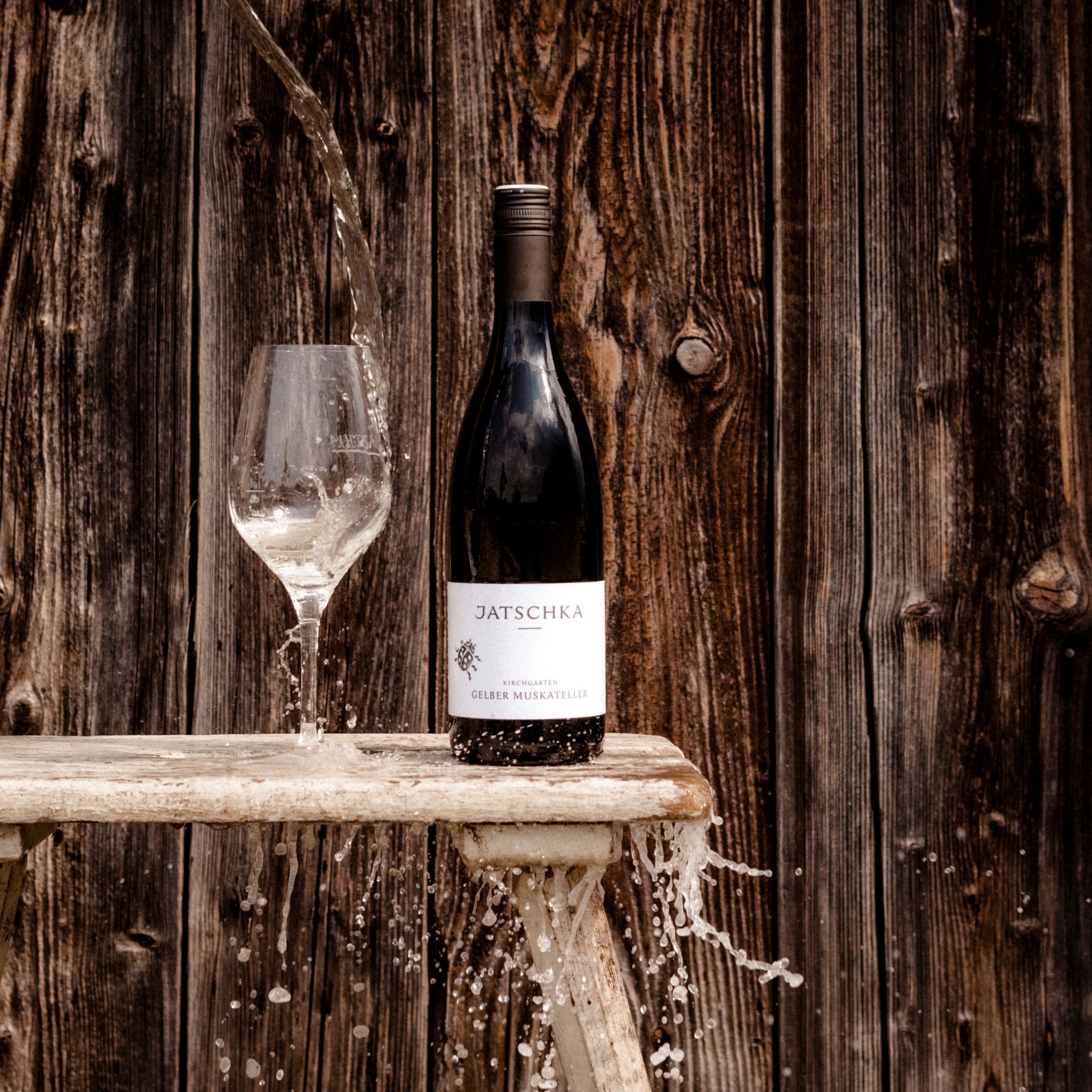 Eine Weinflasche und ein Glas mit Wasser vor einer Holzwand.