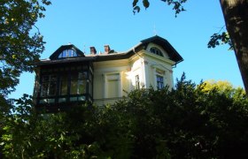 Historische Villa hinter Bäumen, blauer Himmel.