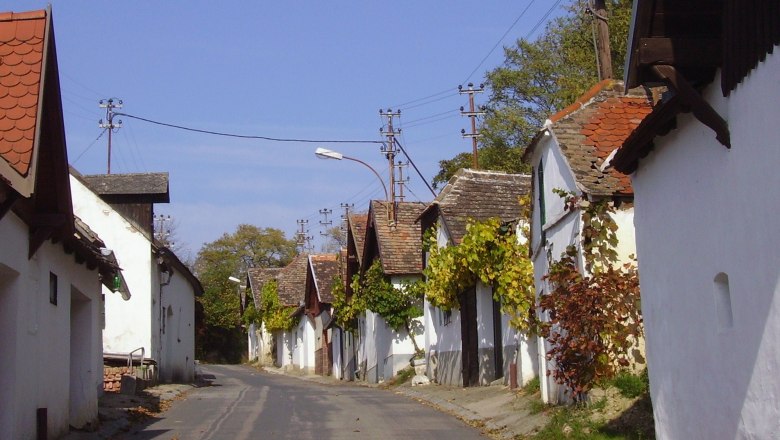 Eine schmale Stra&szlig;e mit traditionellen, wei&szlig;en H&auml;usern und Weinreben an den Fassaden.