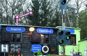 Modelleisenbahn mit Z&uuml;gen vor einem kleinen Geb&auml;ude mit Schildern 'Angertal' und 'Eggenburg'.