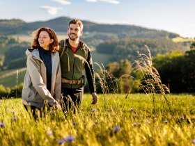 Zwei Wandernde neben einem Getreidefeld mit Kornblumen, im Hintergrund h&uuml;gelige Landschaft mit W&auml;ldern, &copy; Wiener Alpen in Nieder&ouml;sterreich - Bad Erlach