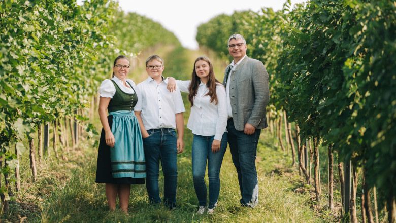 Eine Familie steht lächelnd in einem Weinberg.