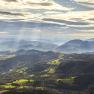 Panoramablick auf die Rax-Alpen mit bewaldeten Hügeln und Sonnenstrahlen durch Wolken.