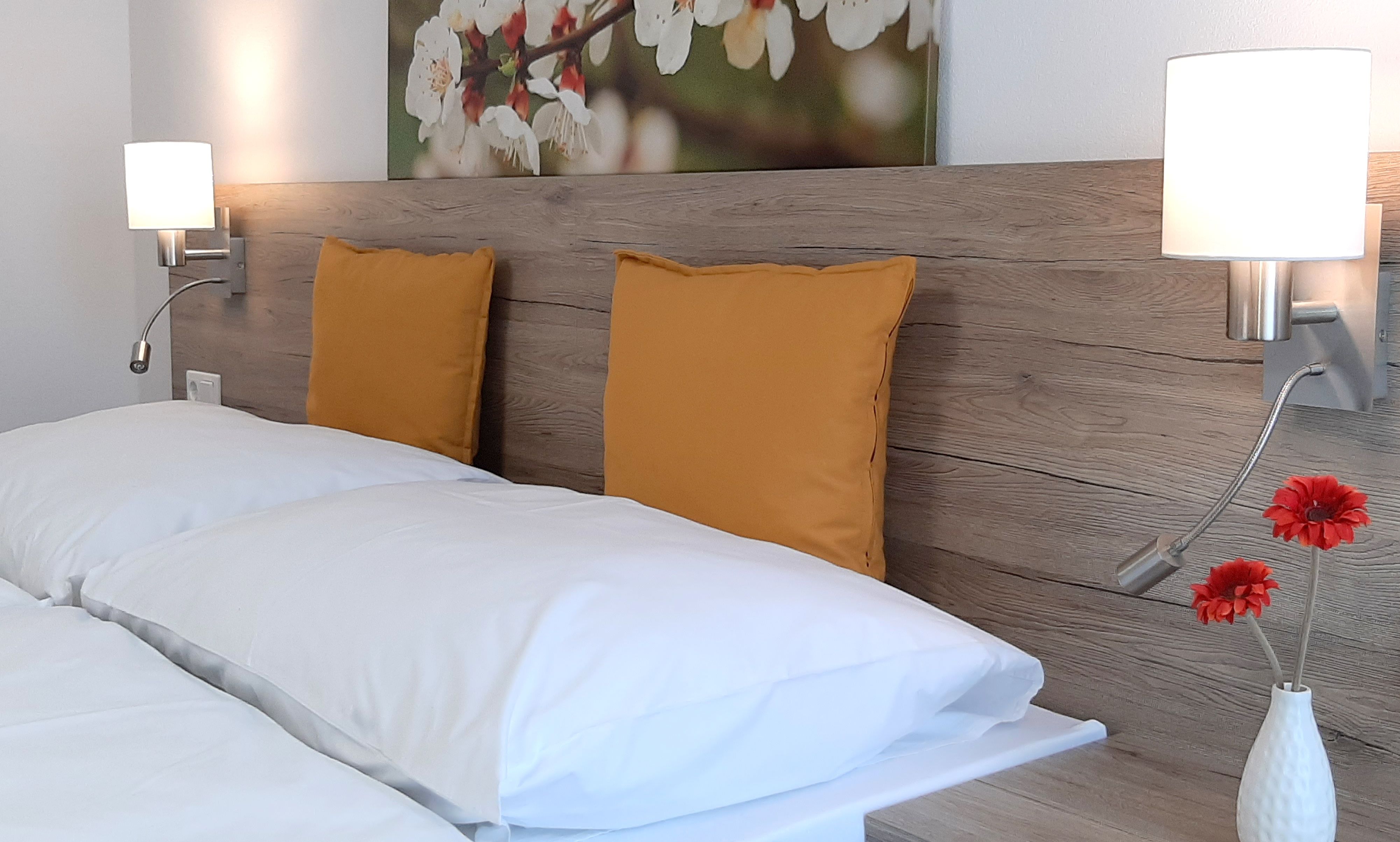 Doppelbett mit Holzrückwand, gelben Kissen und Wandlampen.