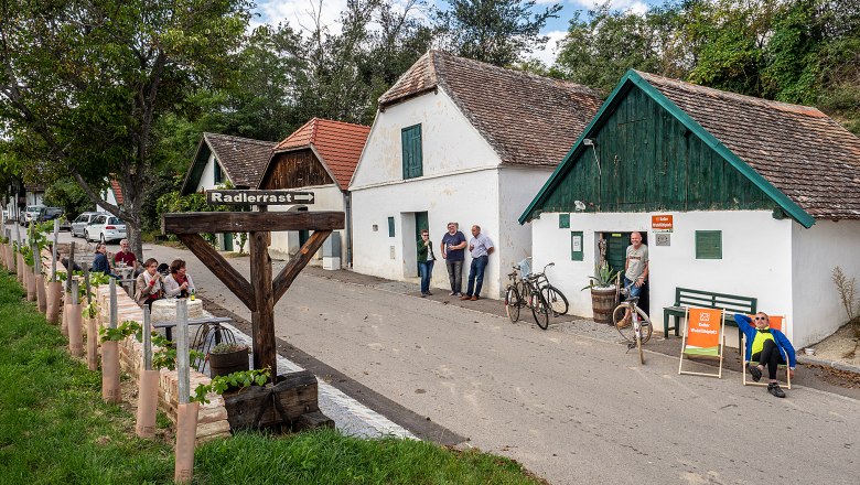 Weinkellerstra&szlig;e in Mailberg mit Menschen, Fahrr&auml;dern und einem Schild 'Radlerrast'.