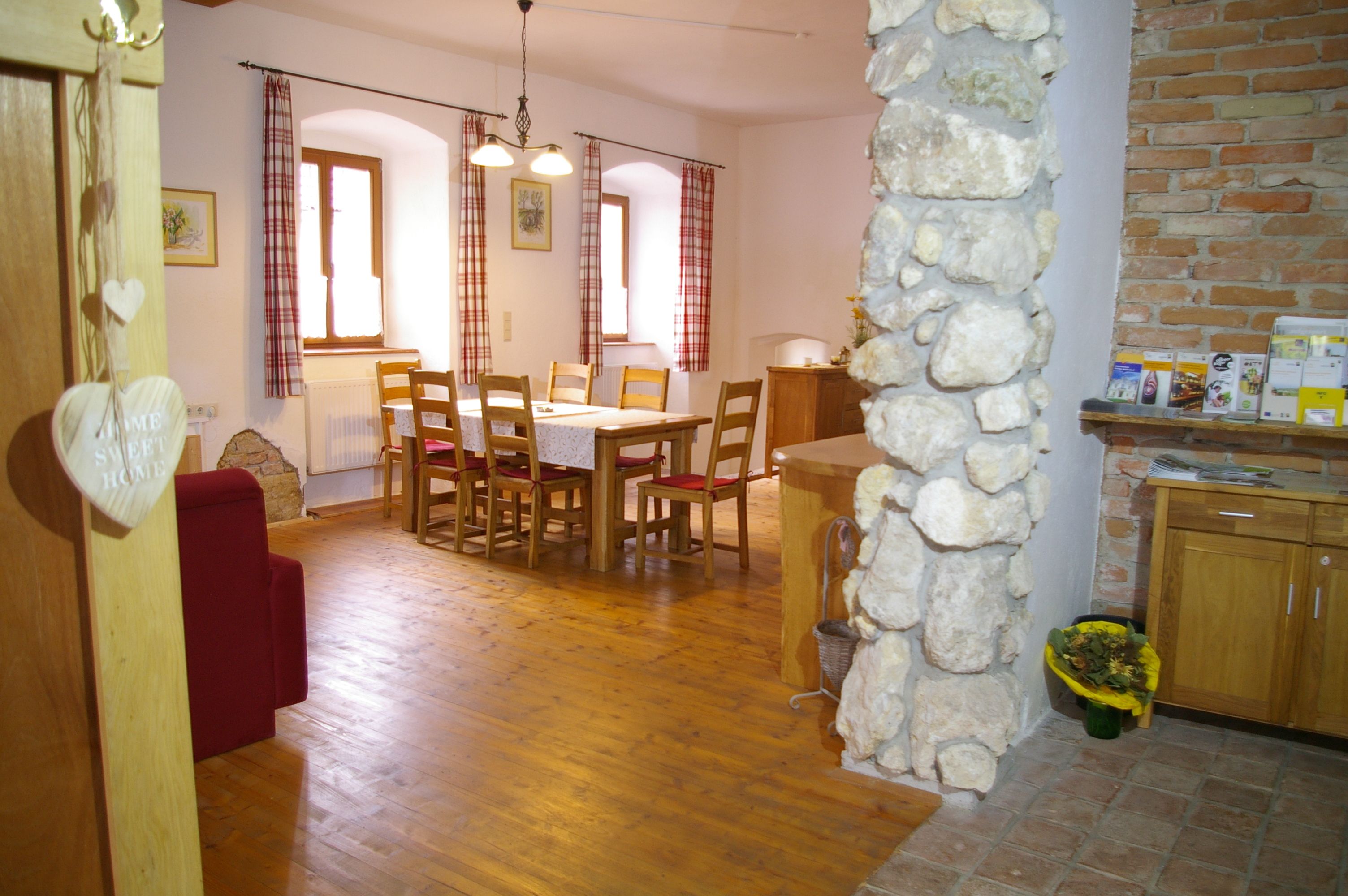 Gemütlicher Essbereich mit Holztisch und Stühlen, roten Vorhängen und Steinmauer.