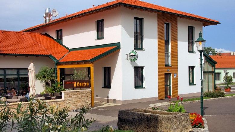 Haus aussen, © Scheumbauer Außenansicht eines Gebäudes mit rotem Dach und Terrasse, beschriftet mit 'caffè e vini Centro'.