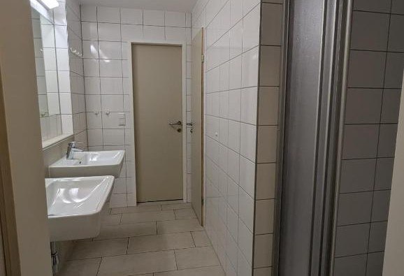 Ein Badezimmer mit zwei Waschbecken, wei&szlig;en Fliesen und einer T&uuml;r.