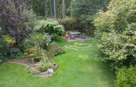 Ein gepflegter Garten mit Rasen, Bäumen und einem Sitzbereich auf einer Terrasse.