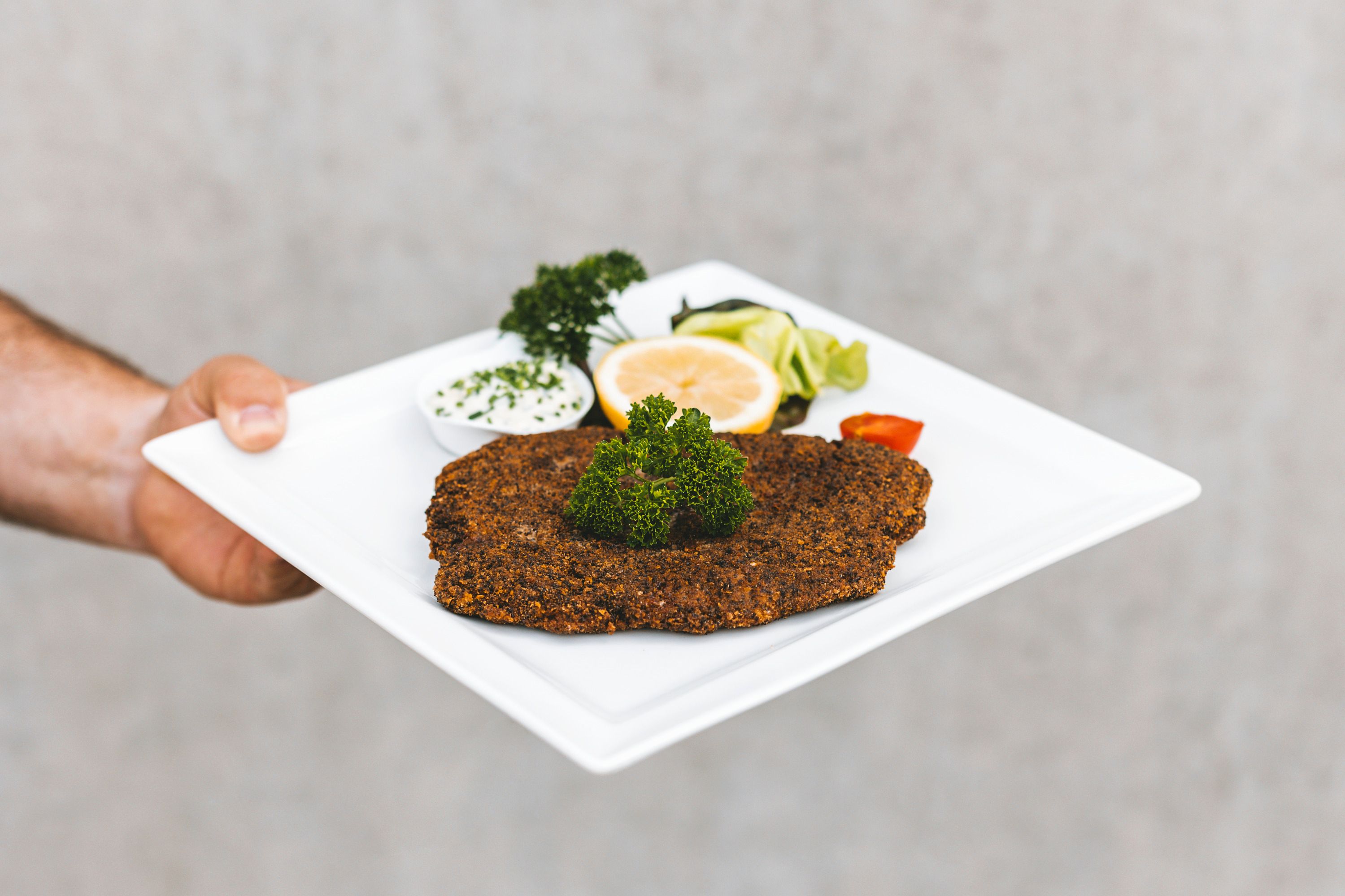 Ein Teller mit paniertem Fisch, Zitrone, Petersilie und Dip.