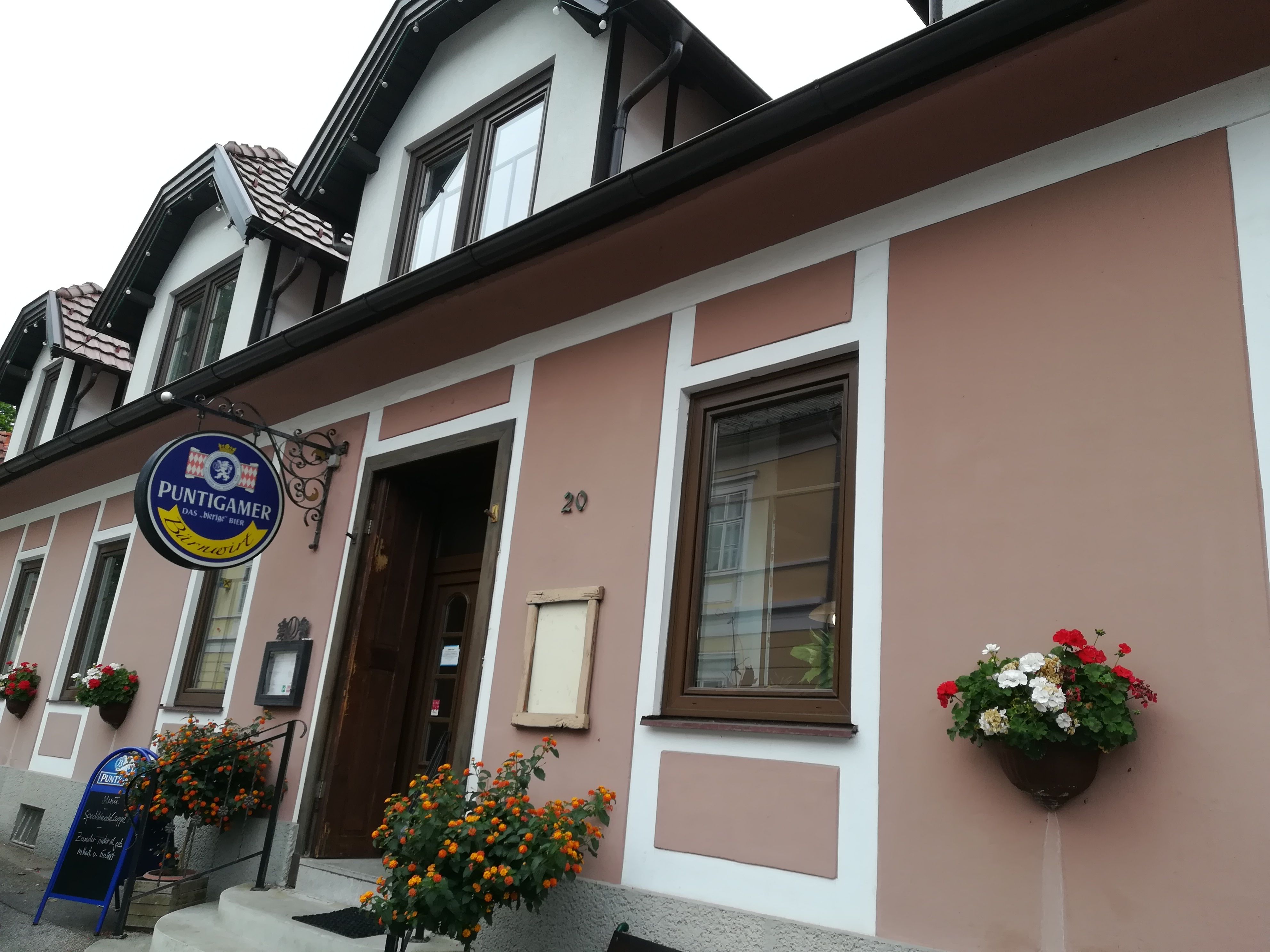 Außenansicht eines Gebäudes mit Schild 'Puntigamer' und Blumendekoration.