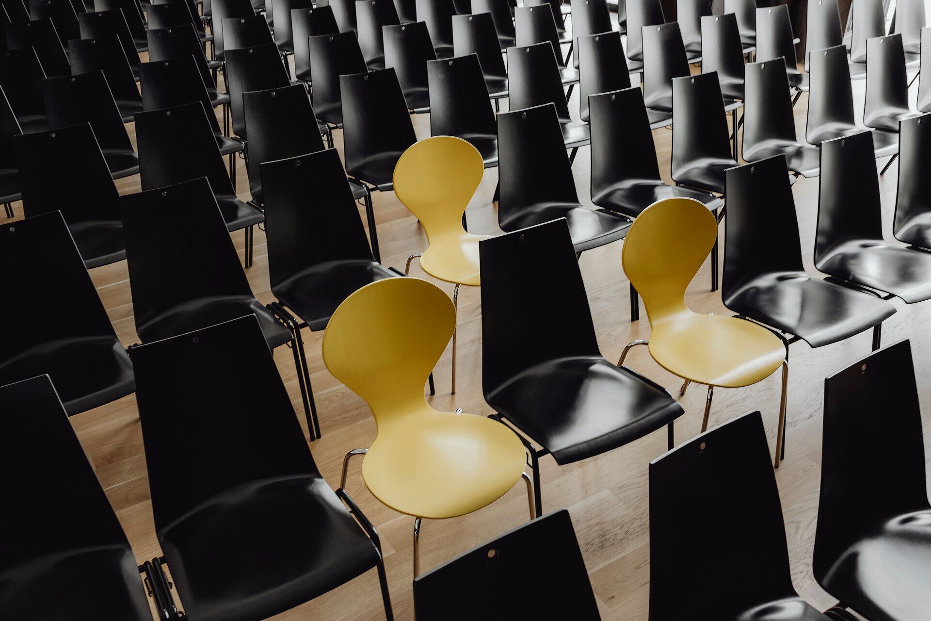 Eine eindrucksvolle Anordnung von Stühlen in einem modernen Veranstaltungsraum schafft eine einladende Atmosphäre für Konferenzen und Events. Die Kombination aus schwarzen und einem gelben Stuhl sorgt für einen frischen, dynamischen Look, der die Vorfreude auf inspirierende Begegnungen und anregende Gespräche weckt.