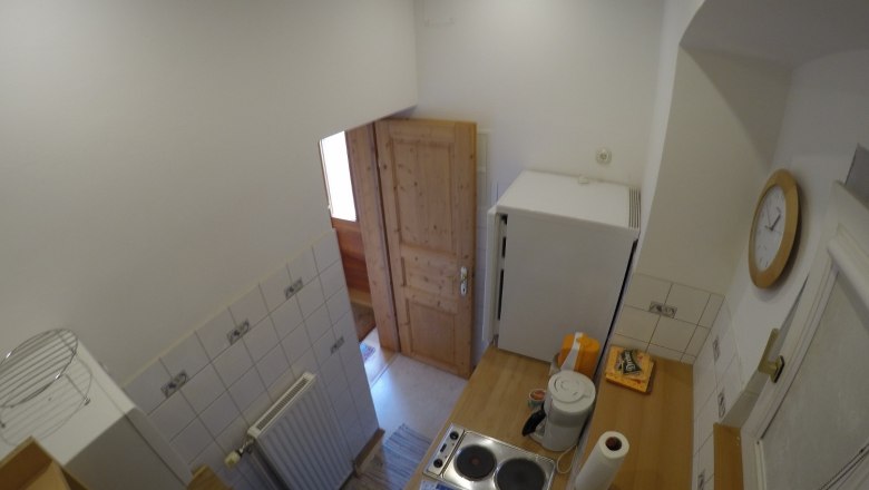 Kleine K&uuml;che mit Herd, K&uuml;hlschrank und Holzt&uuml;r.