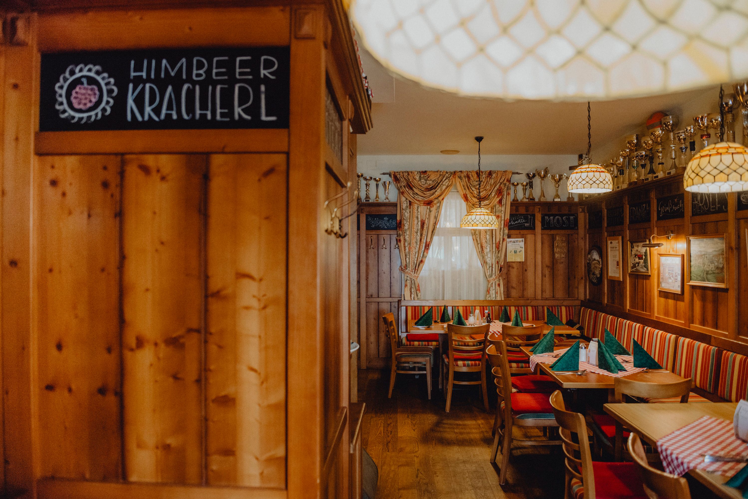 Gemütliche Bauernstube mit Holzmöbeln, karierten Tischdecken und Pokalen auf einem Regal.