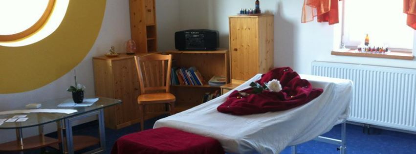 Ein gemütlicher Massageraum mit Massageliege, Holzregalen und einem großen runden Fenster.
