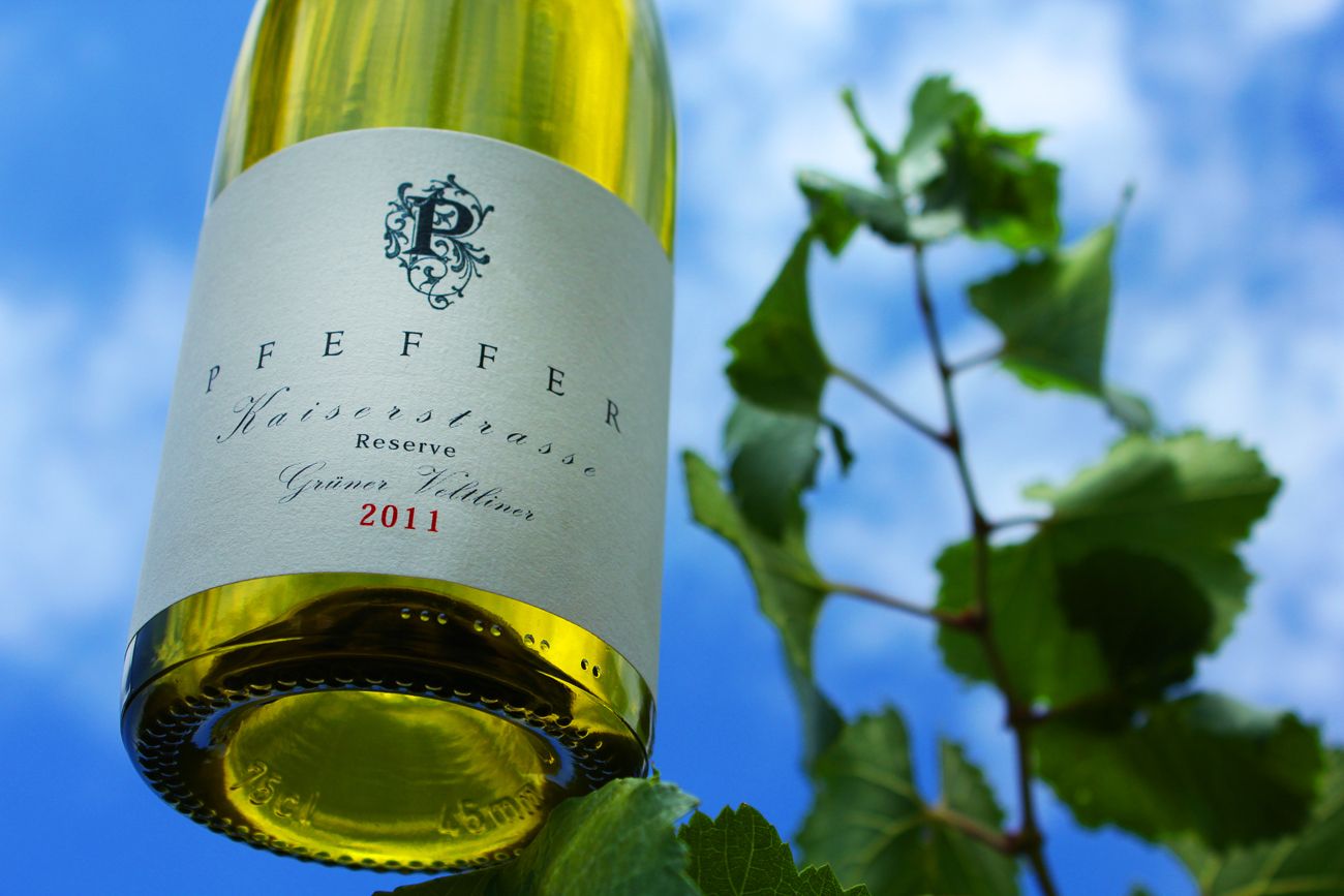 Weinflasche mit Etikett 'Pfeffer Kaiserstrasse Reserve Grüner Veltliner 2011' vor blauem Himmel und Weinblättern.