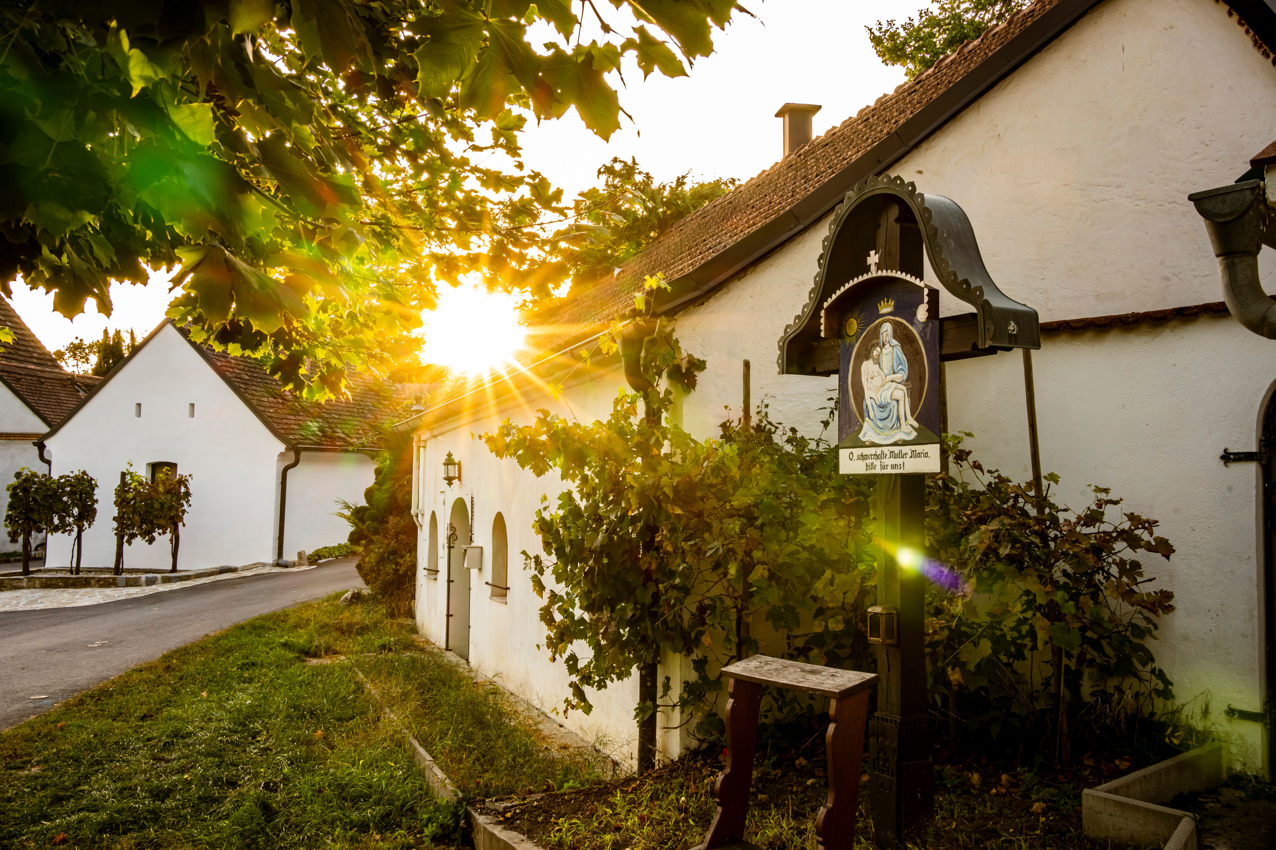 Sonnenuntergang in der Sitzendorfer Kellergasse mit alten Weinkellern und einem religiösen Bildstock.