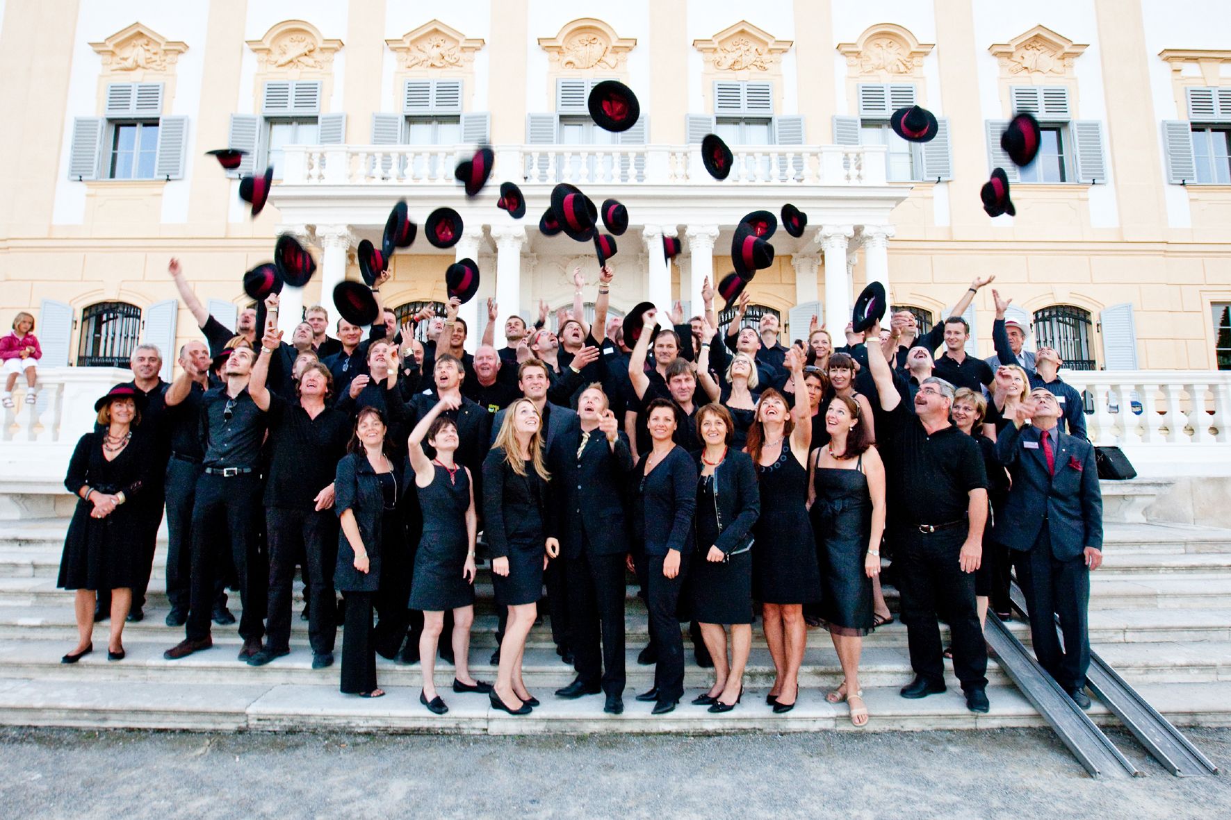 Gruppe von Menschen wirft Hüte in die Luft vor einem historischen Gebäude.