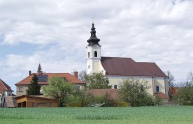 Kirche in Sankt Leonhard am Hornerwald mit umliegenden Geb&auml;uden und gr&uuml;nem Feld.